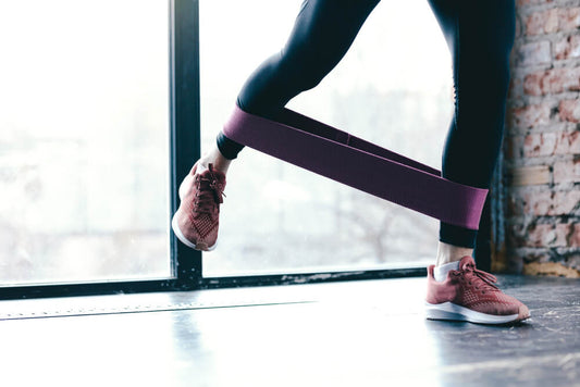 Photo of a woman using resistance bands on her lower legs to illustrate Exersci blog post entitled 'Can I Build Muscle With Resistance Bands?'.  